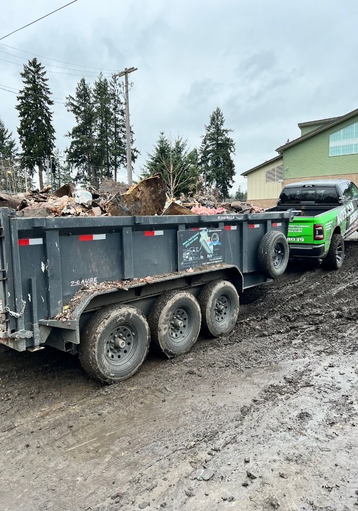 Triple-axle dump trailer filled with demolition debris, hitched to a branded Nate’s Junk Removal truck on a job site in Washington